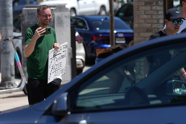 ▲ 덴마크의 토르킬드 요한센이 22일(현지시간) 텍사스 오스틴에서 무인 테슬라 로보택시, 차량 예약 서비스 사진을 찍고 있다. 사진=뉴시스