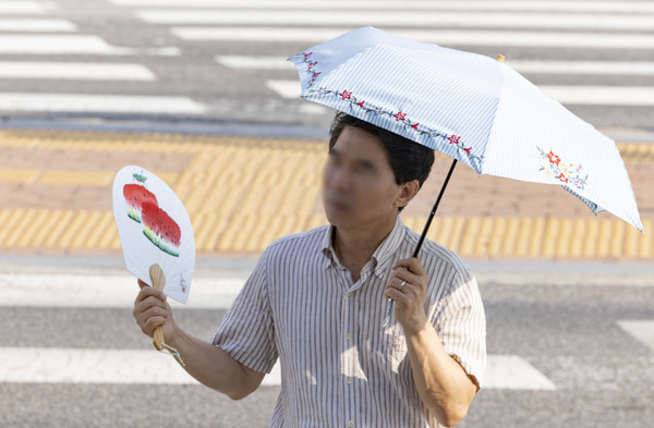 ▲ 서울 서초구 고속버스터미널 인근에서 한 시민이 부채로 더위를 식히며 양산을 쓴 채 출근길에 나서고 있다. 사진=뉴시스